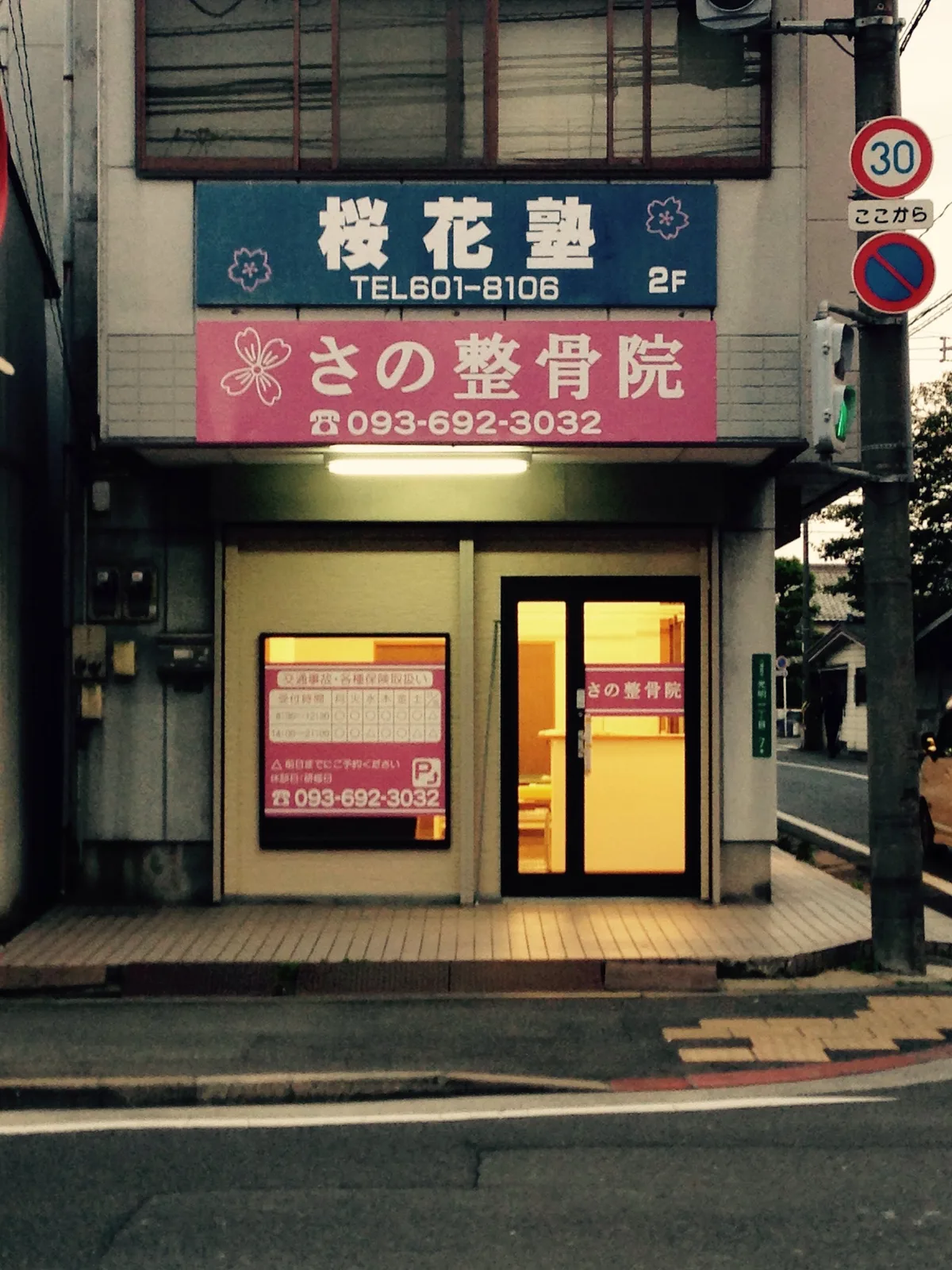 さの整骨院の外観。桜のマークとピンク色の看板、1階が入口
